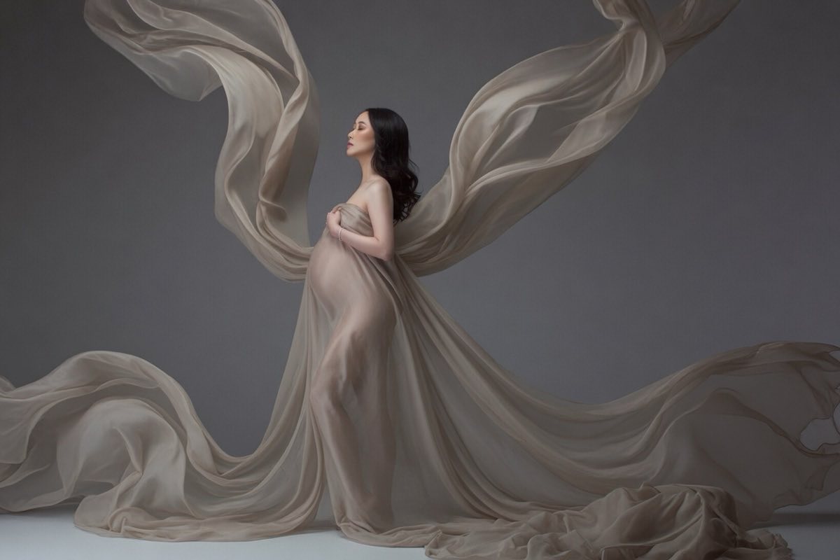 Pregnant woman framed by flowing neutral fabric during a studio maternity portrait