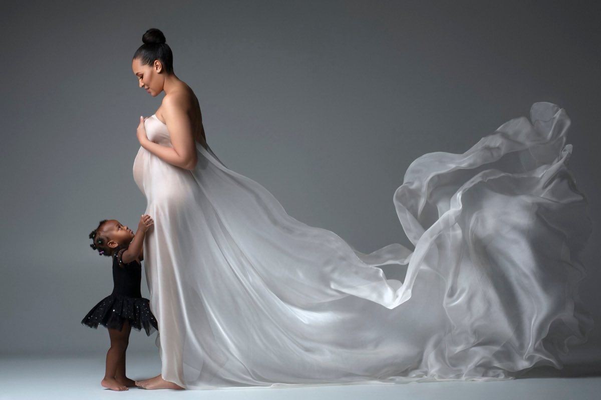 Pregnant mother and young daughter in flowing studio fabric during a maternity portrait