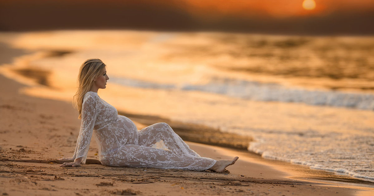Pregnant woman in a white lace gown on a Chicago beach at sunset