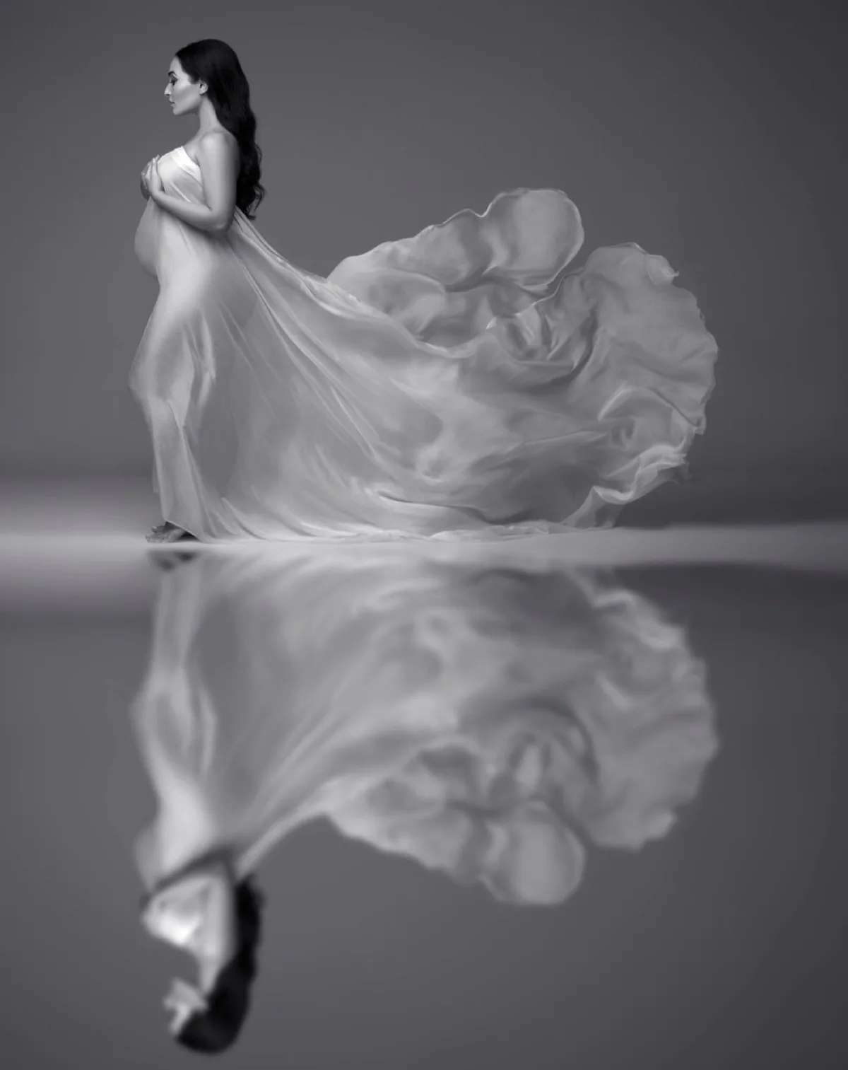 Fine-art maternity silhouette framed by flowing white silk